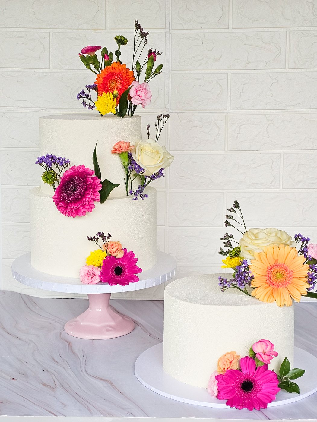 Two white cakes with fresh gerberas, carnations and roses