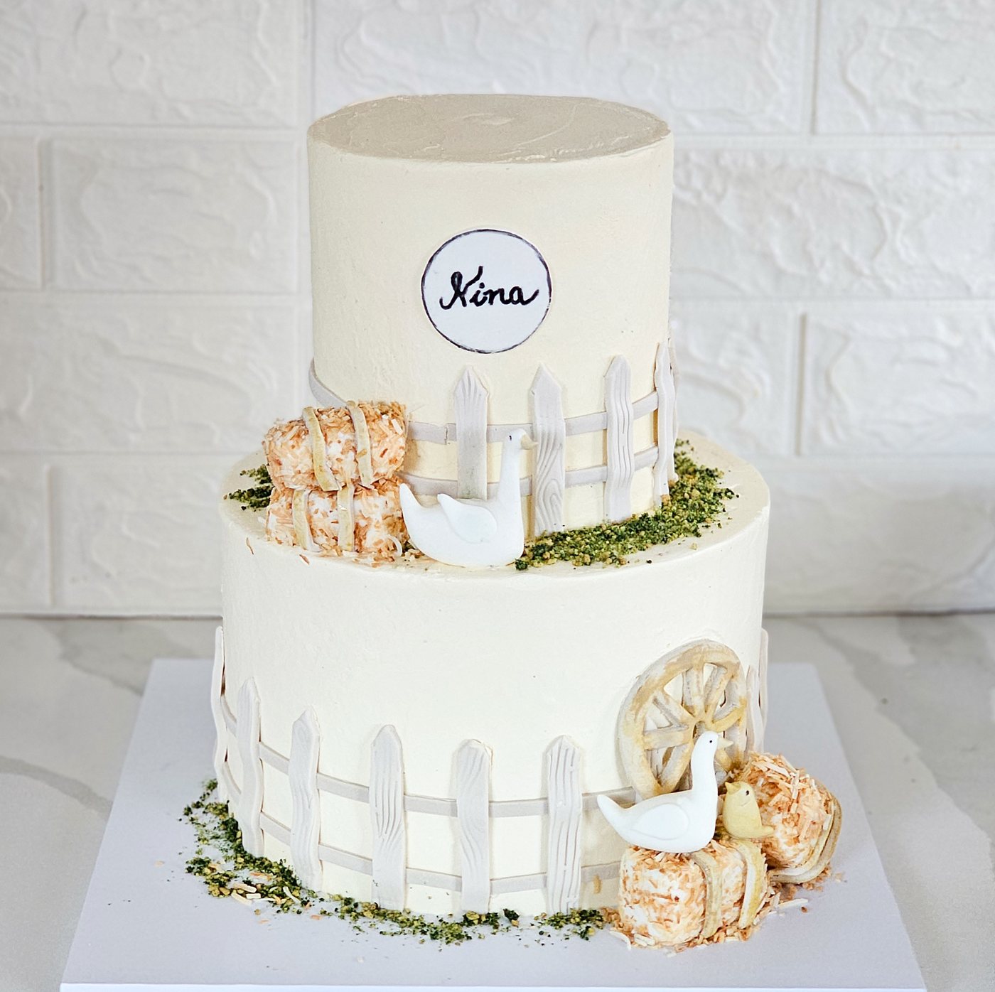 Two tier white farm cake with a picket fence, hay bales and a goose