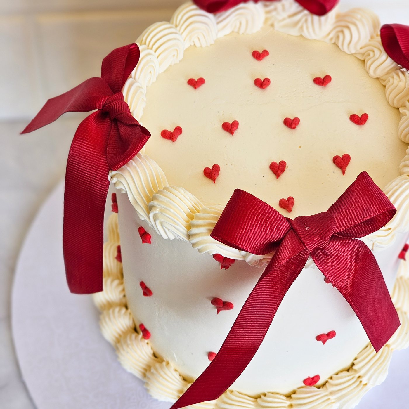 White cake with red hearts, piped borders and red satin bows